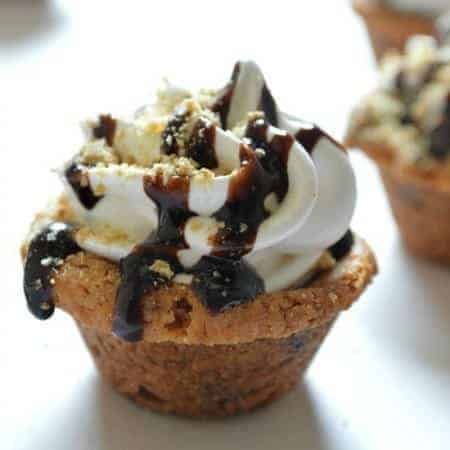 S'mores Cups. Chocolate chip cookie cups topped with chocolate, the fluffiest Marshmallow frosting EVER and graham cracker crumbs! YUM!! #smoresweek