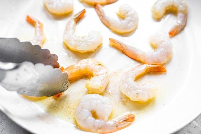 Tongs turning shrimp to cook in a skillet.