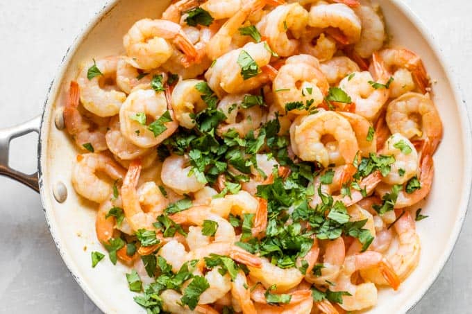 Chopped cilantro being added to cooked shrimp.