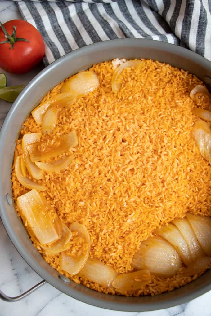 A large skillet filled with Mexican Rice and quartered onion ready to fluff with a fork. 