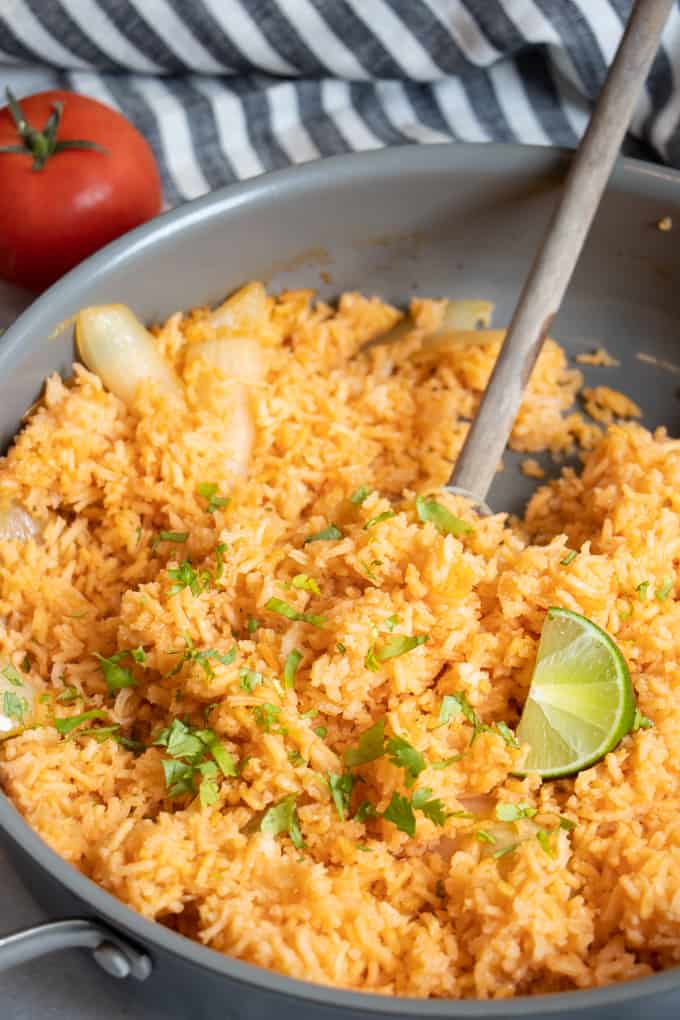 Large skillet, showing Mexican Rice being served with a wooden spoon. 