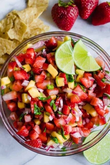 Bowl full of strawberry mango salsa topped with lime wedges.
