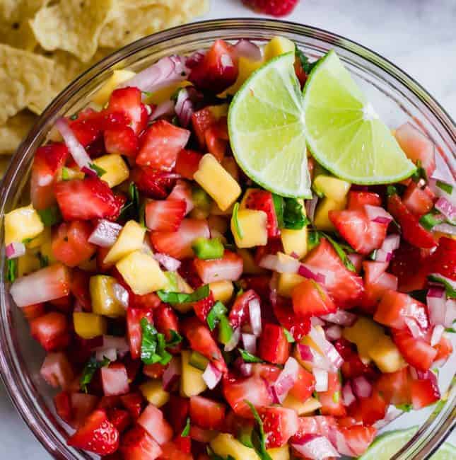 Bowl full of strawberry mango salsa topped with lime wedges.