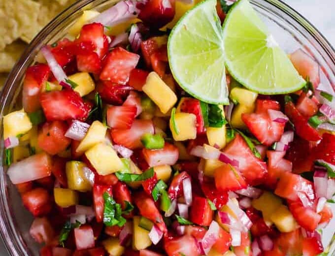Bowl full of strawberry mango salsa topped with lime wedges.