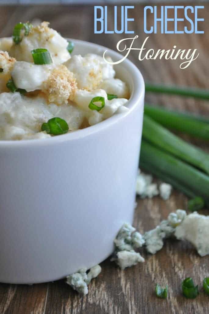Blue cheese hominy in a bowl surrounded by crumbled blue cheese and diced green onion. 
