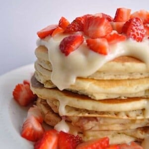 Stack of pancakes topped with cream cheese glaze and cut strawberries.