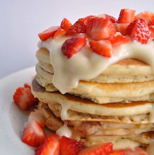 Stack of pancakes topped with cream cheese glaze and cut strawberries.