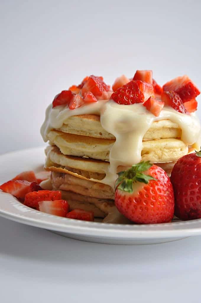 Cream cheese glaze dripping down the sides of pancakes with diced strawberries on top.