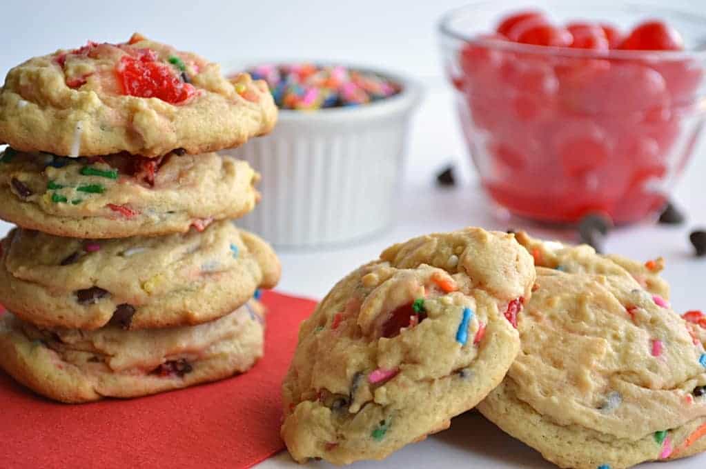 Stack of banana pudding cookies with sprinkles and cherries on a red napkin.