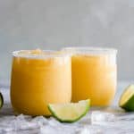 Frosty mango margarita in a glass rimmed with sugar and lime wedges.