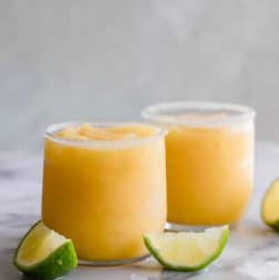 Frosty mango margarita in a glass rimmed with sugar and lime wedges.