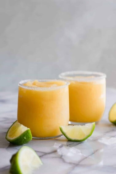 Frosty mango margarita in a glass rimmed with sugar and lime wedges.