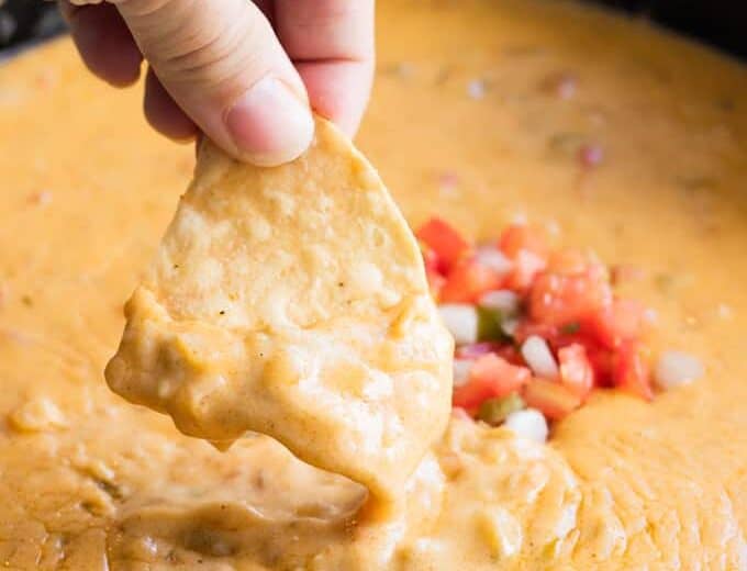 A chip dipping into homemade queso.