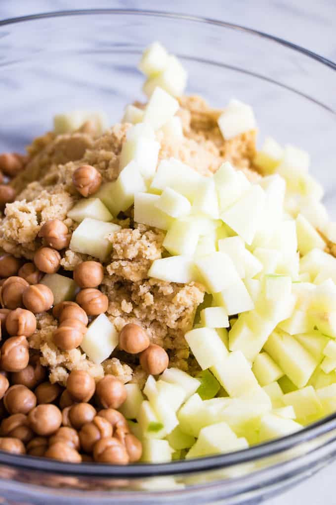  Un bol rempli de pâte à biscuits garni de morceaux de caramel et de pommes hachées pour faire des biscuits aux pommes au caramel.