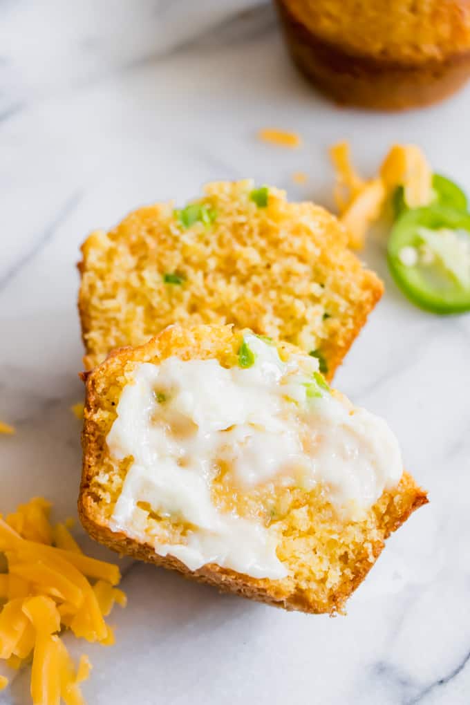 Jalapeno Cheddar Cornbread muffin split apart with sweet honey butter spread on top.
