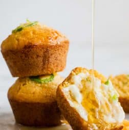 Stacked Jalapeno Cheddar Cornbread muffins, with one cut open and smeared with a sweet honey butter and a honey drizzle running down.