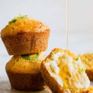 Stacked Jalapeno Cheddar Cornbread muffins, with one cut open and smeared with a sweet honey butter and a honey drizzle running down.