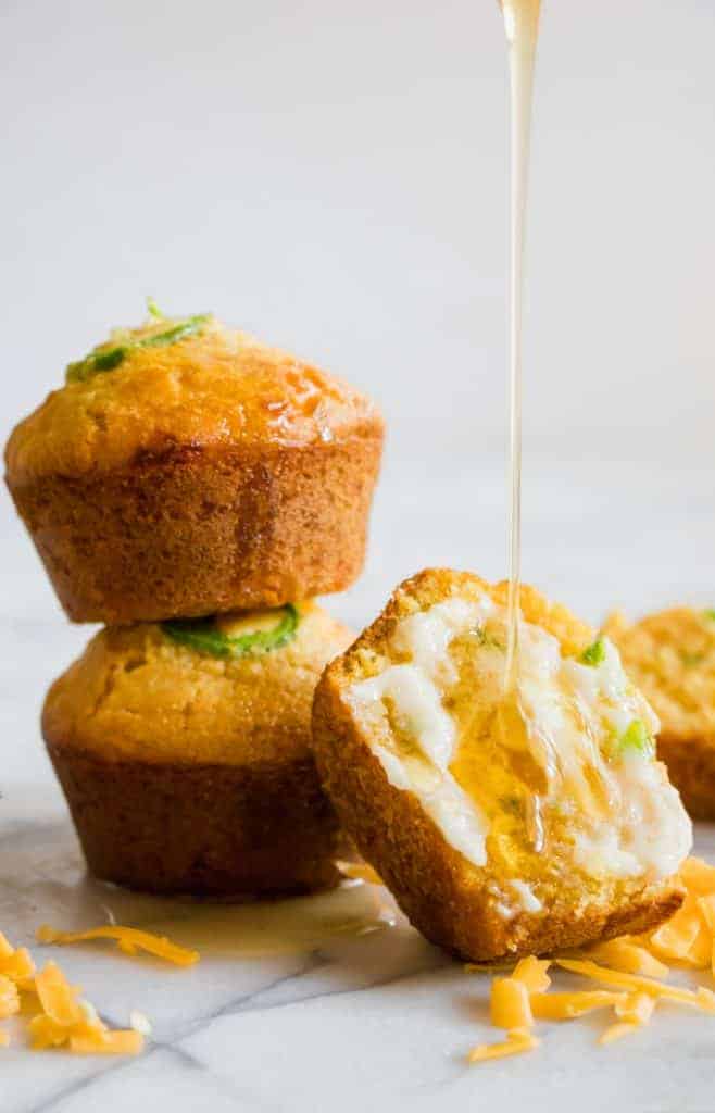 Stacked Jalapeno Cheddar Cornbread muffins, with one cut open and smeared with a sweet honey butter and a honey drizzle running down.