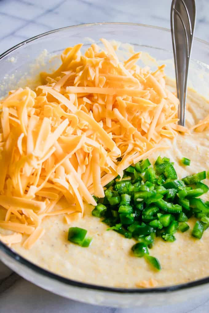 A bowl of cornbread batter topped with shredded cheese and diced jalapeno. 