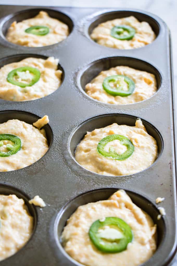 Jalapeno Cheddar Cornbread batter in a muffin tin, topped with a slice of jalapeno.