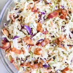 Large glass bowl filled with creamy blue cheese coleslaw topped with bacon.