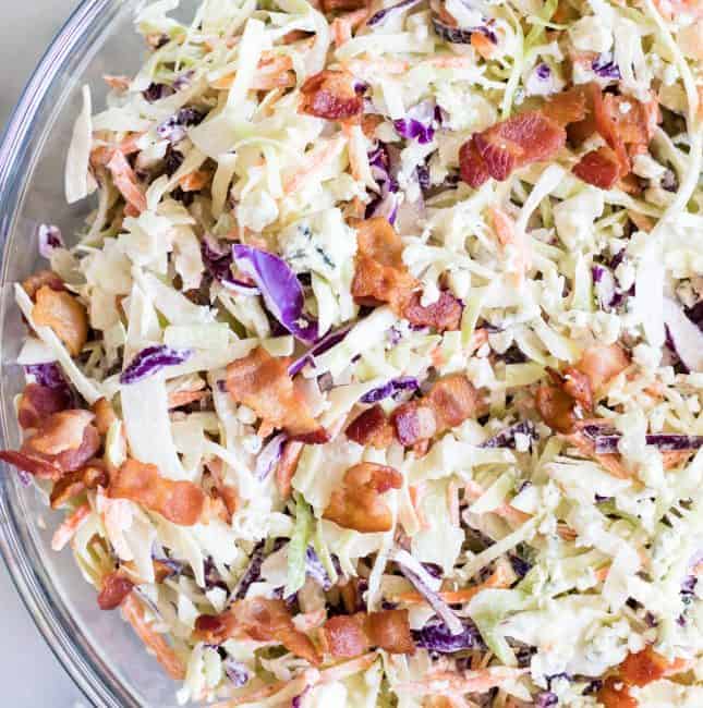 Large glass bowl filled with creamy blue cheese coleslaw topped with bacon.