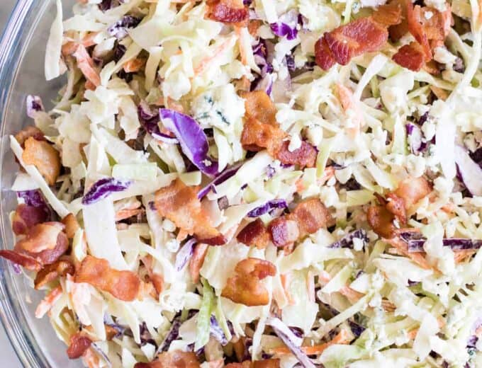 Large glass bowl filled with creamy blue cheese coleslaw topped with bacon.