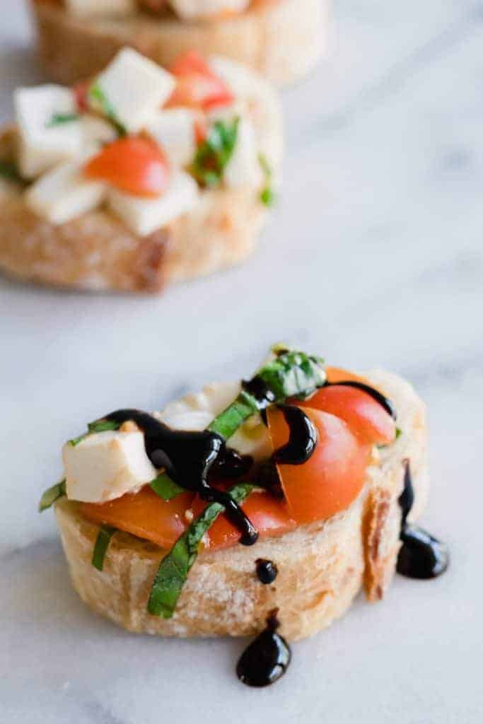 Caprese Bruschetta em cima de baguete fatiado e regado com um glace balsâmico.