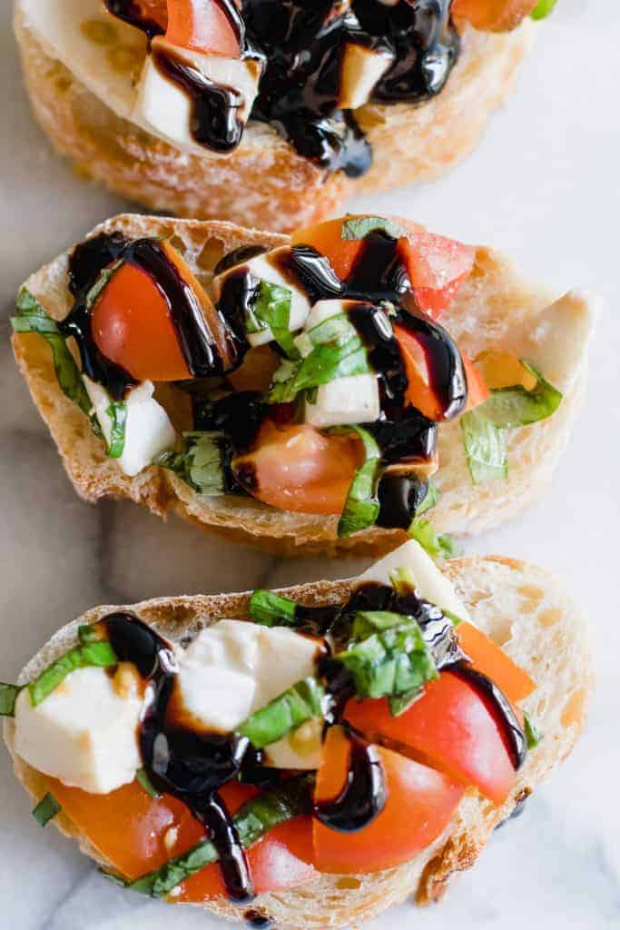 Overzicht van caprese bruschetta besprenkeld met een balsamico glazuur.