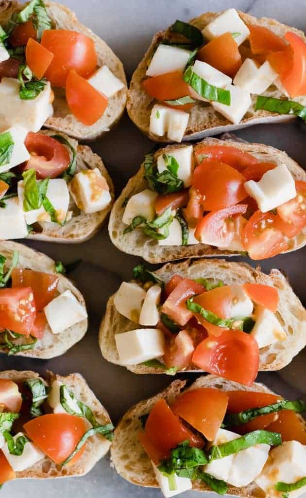 Bread slices laid out and topped with caprese bruschetta, fresh tomatoes, mozzarella and basil.