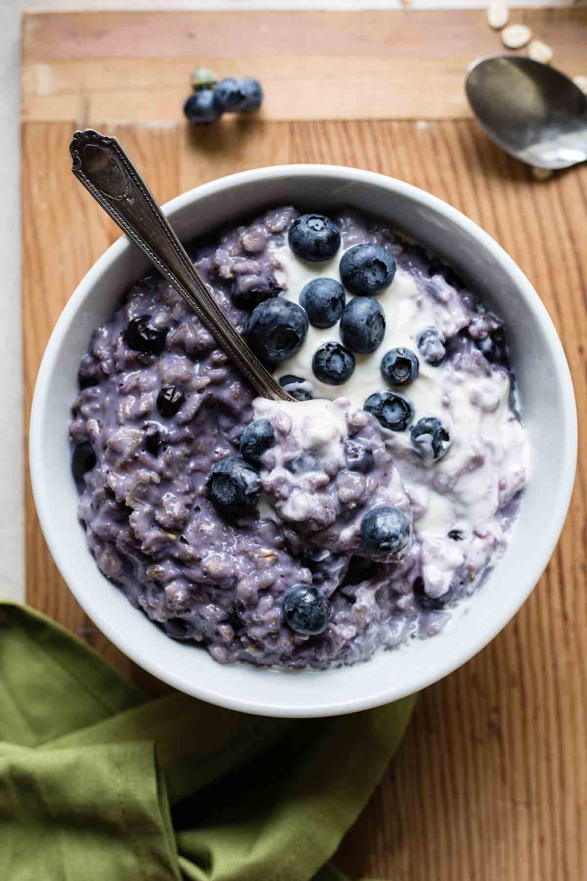 Bowl filled with purple colored blueberry oatmeal, topped with cream and fresh blueberries.