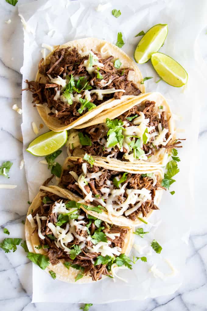 Corn tortillas loaded up with slow cooker sweet barbacoa, topped with melty cheese and chopped cilantro.