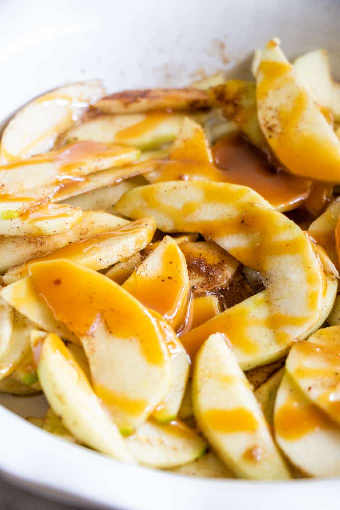 Apples drizzled with caramel to make a caramel apple crisp.