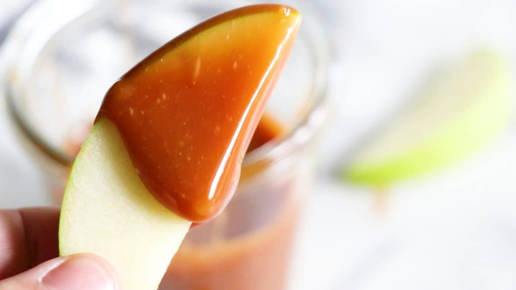 A slice of apple dipped in homemade caramel sauce. 