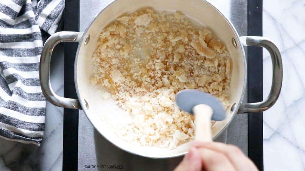 A pot filled with sugar that is starting to melt and form clumps, part of the process of making homemade caramel. 