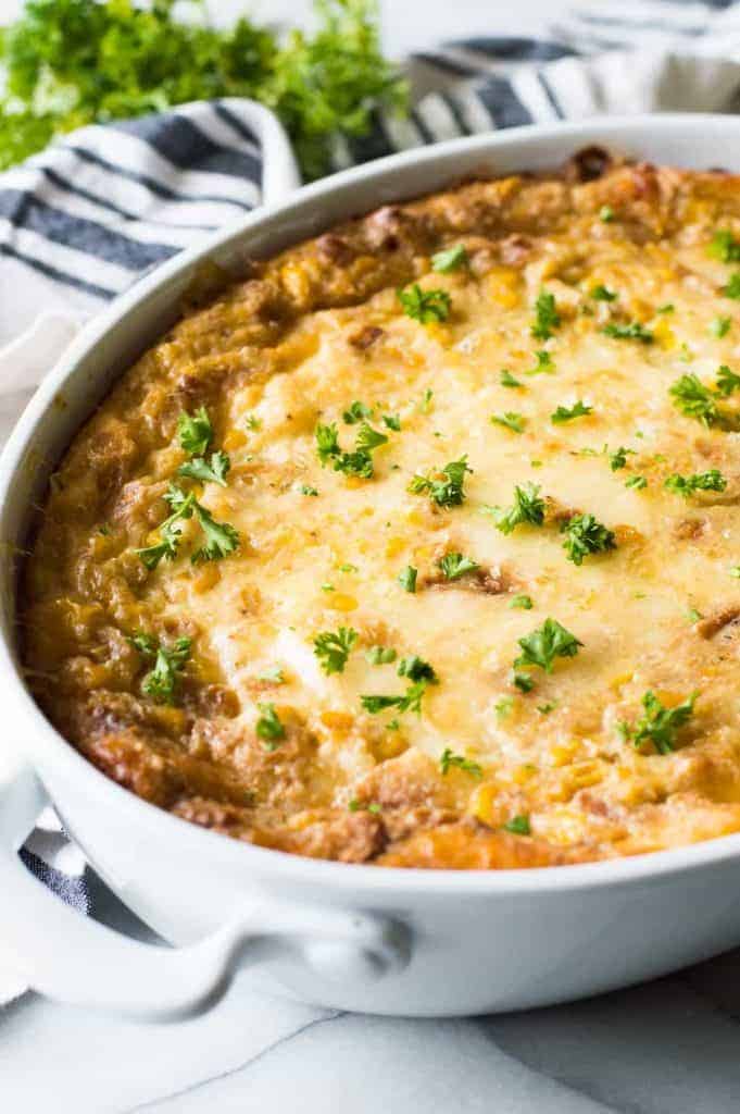 Corn casserole or corn pudding in a casserole dish, topped with fresh parsley.