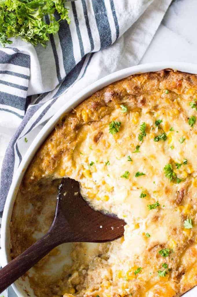 A spoon scooping into a casserole dish of cheesy corn casserole.