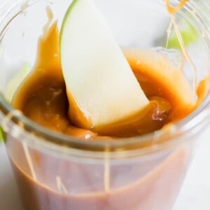 A jar filled with homemade caramel and an apple dipped in.