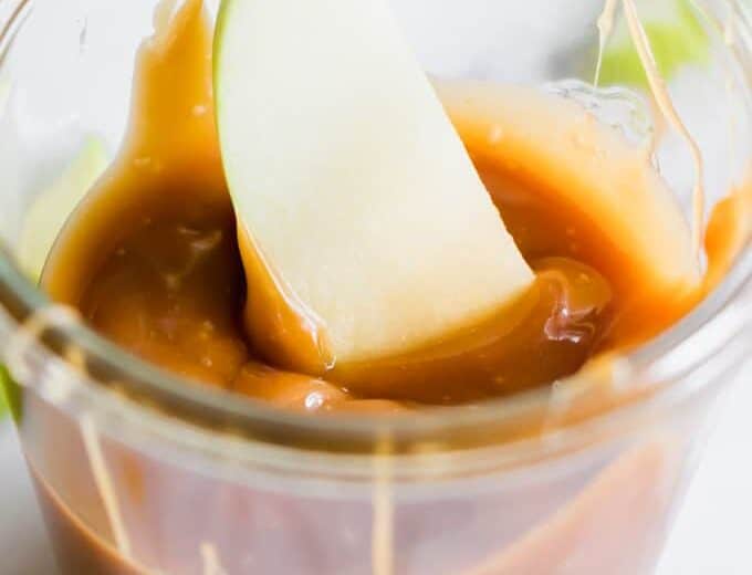 A jar filled with homemade caramel and an apple dipped in.