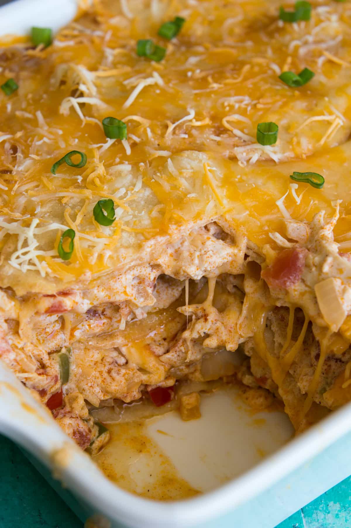 Casserole dish filled with King Ranch Chicken, showing a slice missing and layers of tortillas with a creamy chicken mixture, strings of cheese connecting it all. 