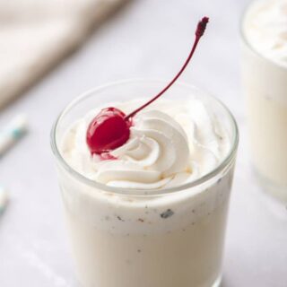 Glass filled with warm vanilla tres leches milk drink. Topped with whipped cream and a cherry.