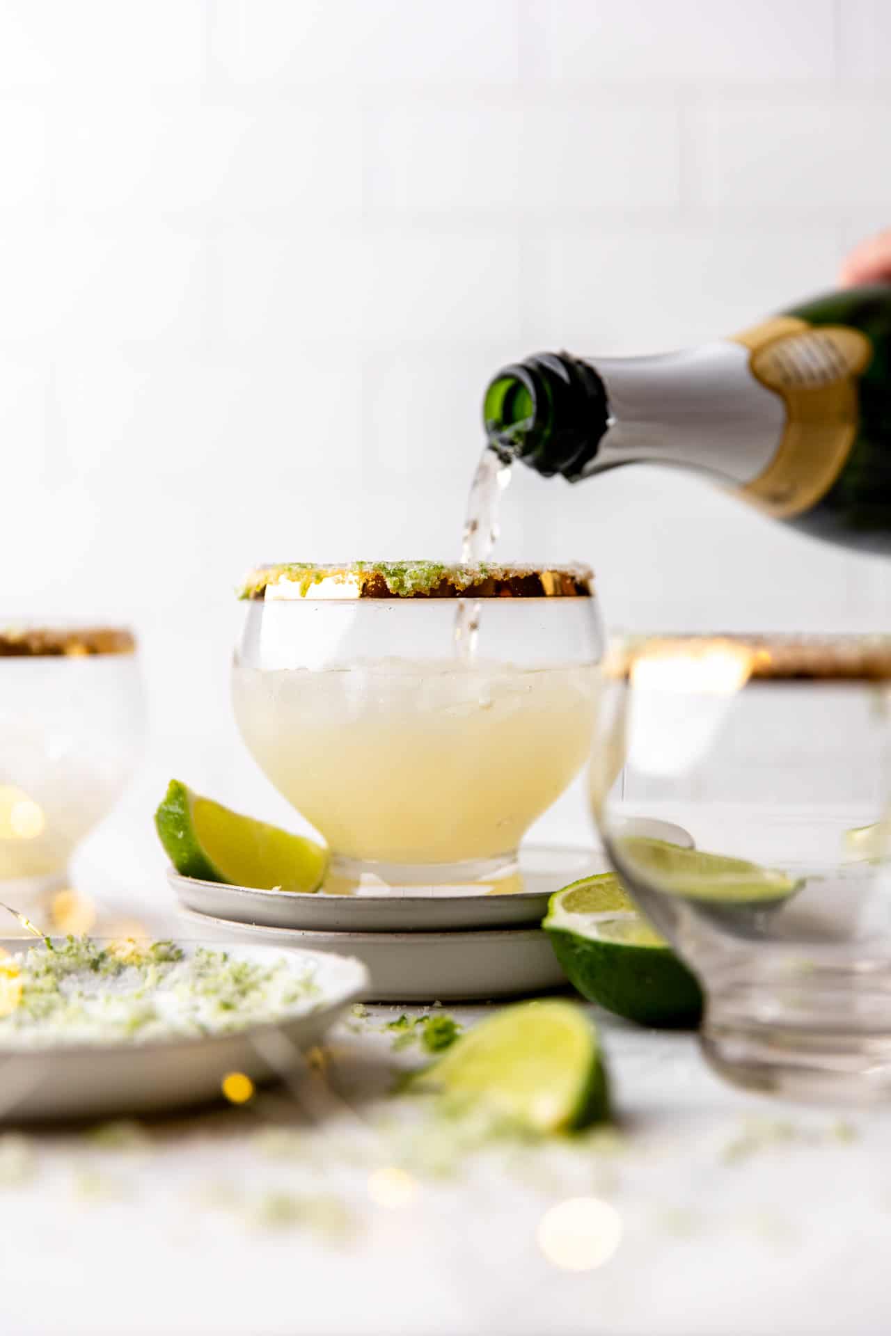 Pouring champagne into gold rimmed glasses with lime zest sugar on the rim. 