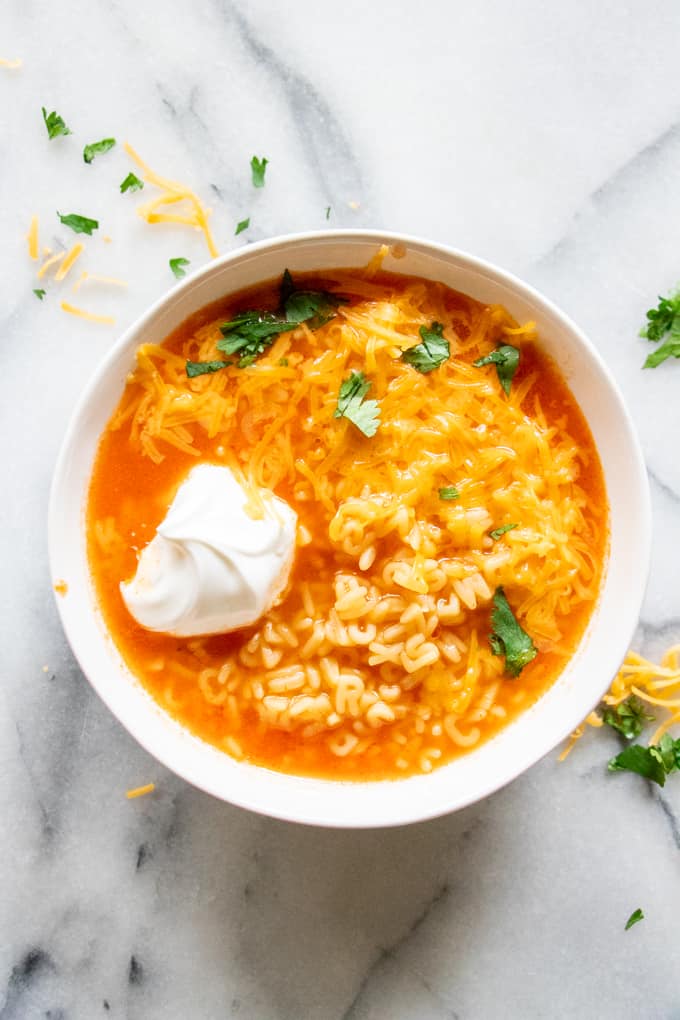 Bowl of Mexican alphabet soup garnished with cheese and cilantro.