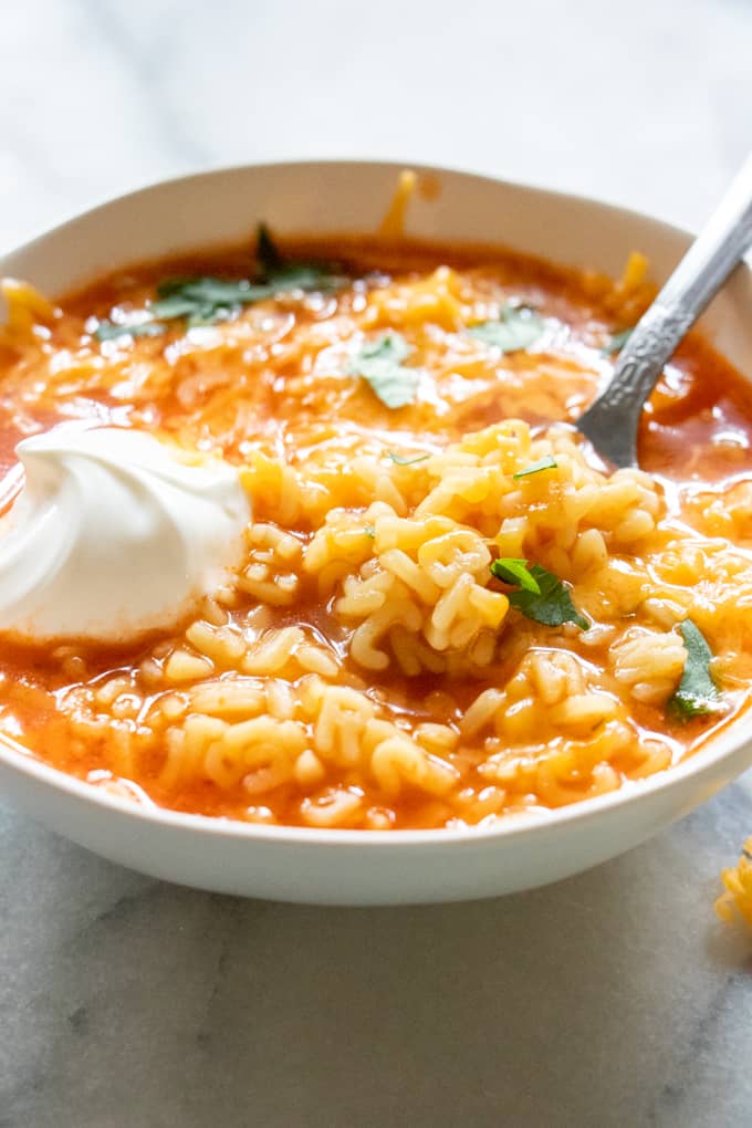 Bowl filled with Mexican alphabet soup topped with a swirl of sour cream.