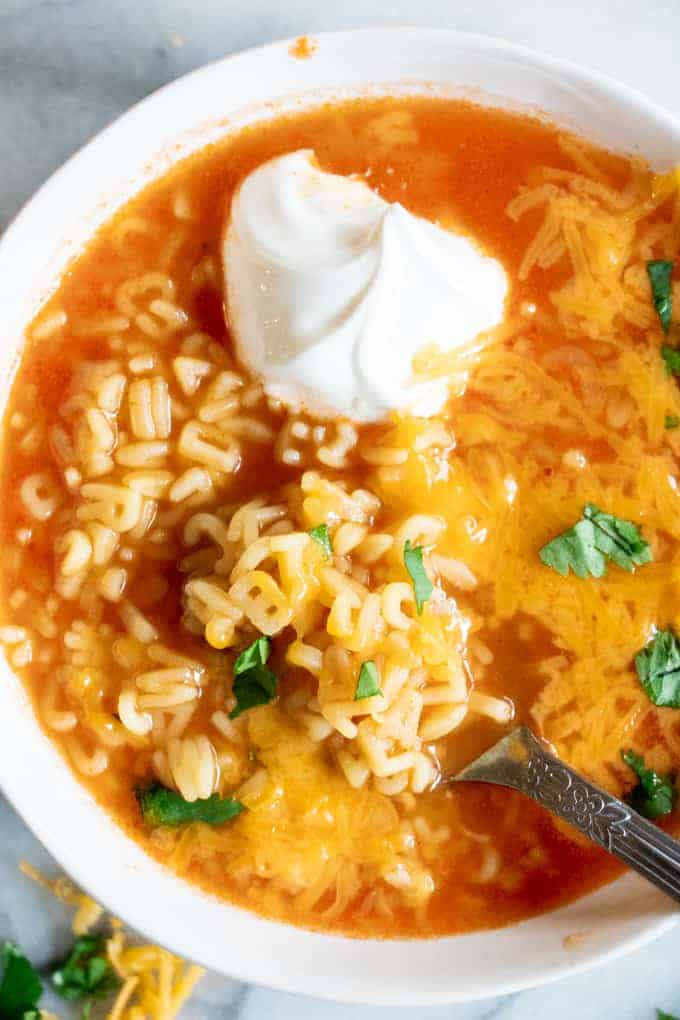 Bowl filled with Mexican Alphabet Soup, sopa de letras, and topped with sour cream, cheese and cilantro. 