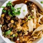Bowl filled with Easy Taco Soup topped with sour cream, cilantro, tortilla strips and melty cheese.