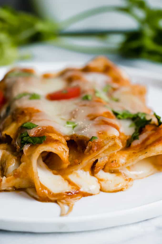 tři sýrové enchiladas podávané na talíři ukazující roztavený bílý sýr vytékající z tortilly.