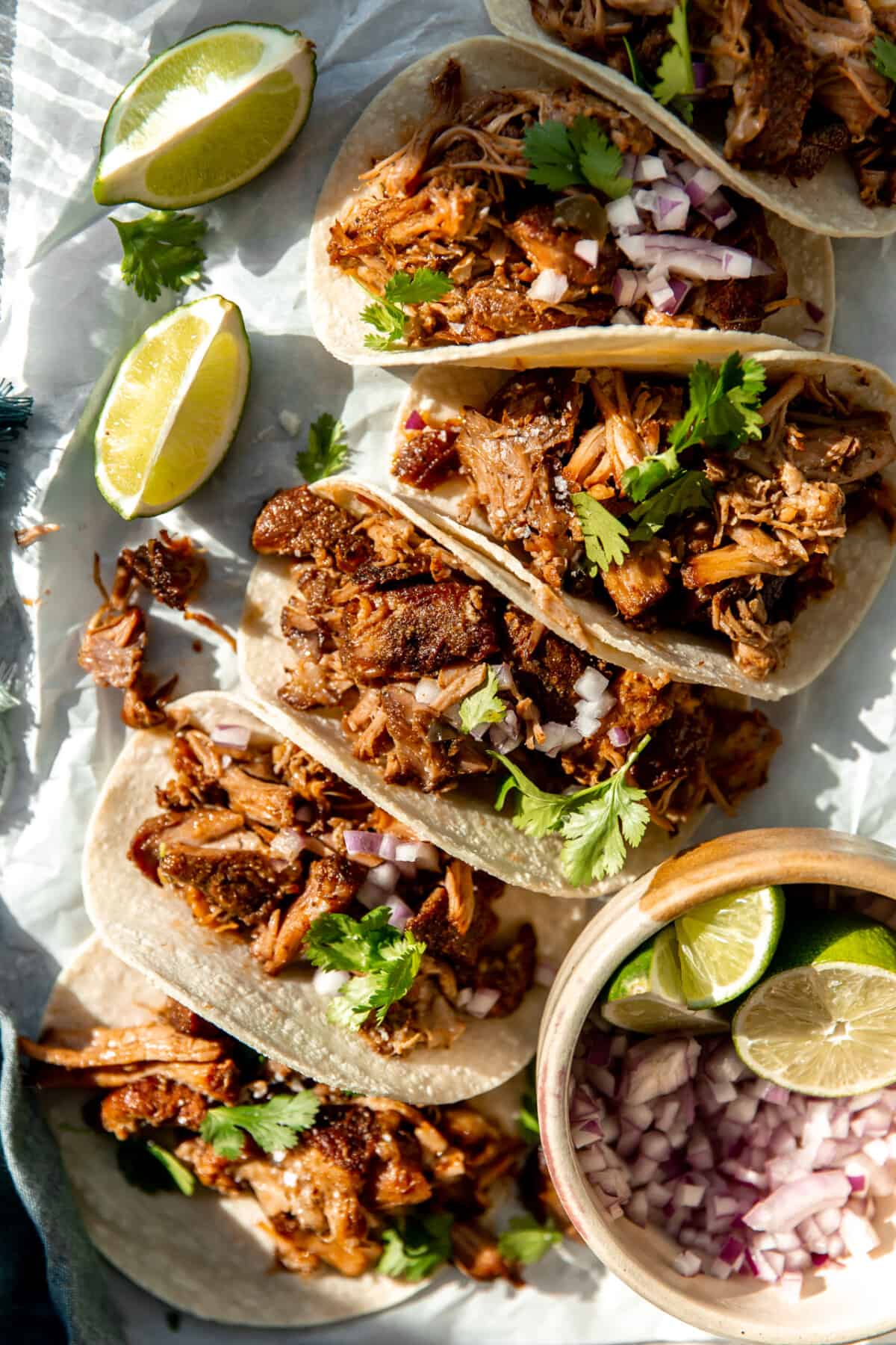 Tortillas lined up with crispy pork carnitas and topped with red onion and fresh cilantro. 