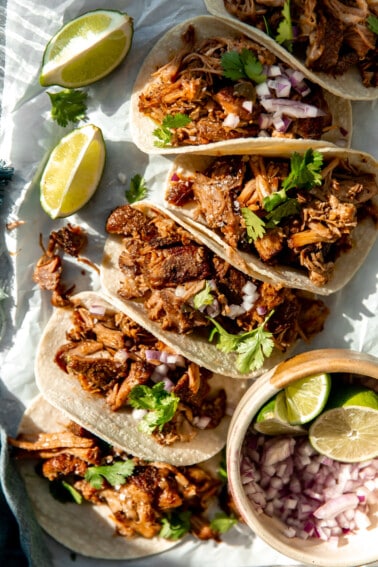Tortillas lined up with crispy pork carnitas and topped with red onion and fresh cilantro.