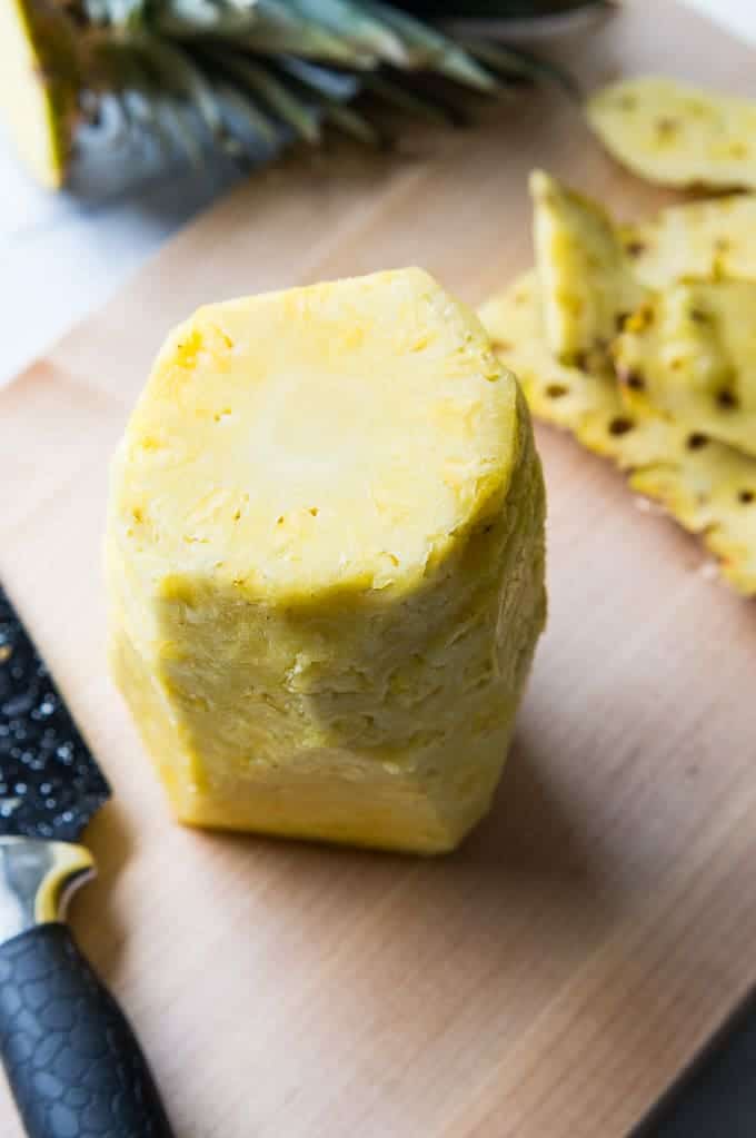 Whole pineapple with the skin removed on a cutting board.